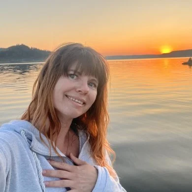 Christina Johnson by a lake at sunset, one hand on her heart