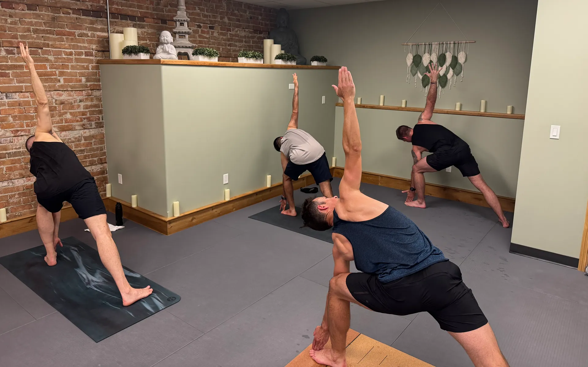 Four students in triangle pose with one arm reaching to the ceiling, the studio’s Buddha shelf behind them