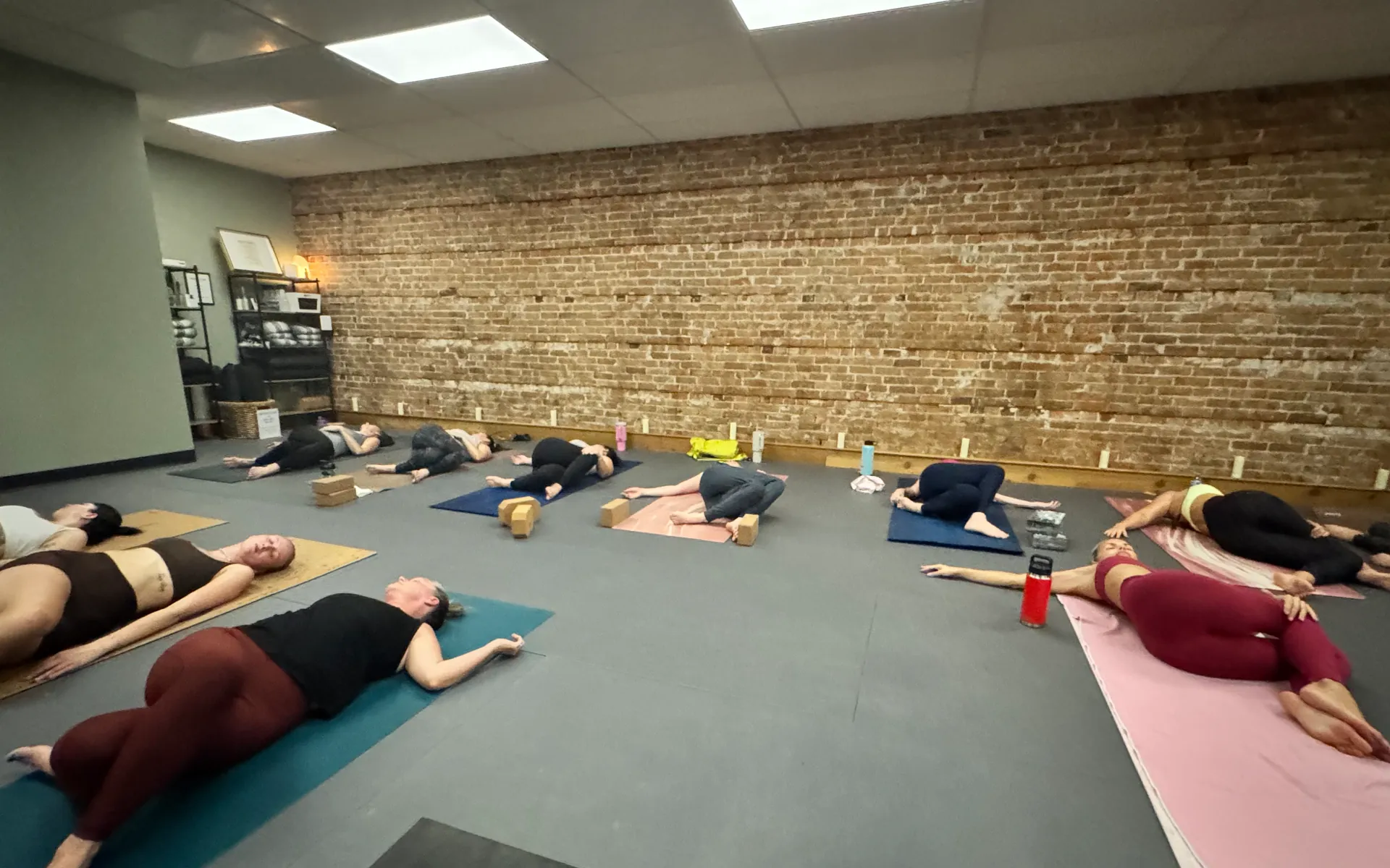 A class lying in a reclined twist on their mats beside the brick wall